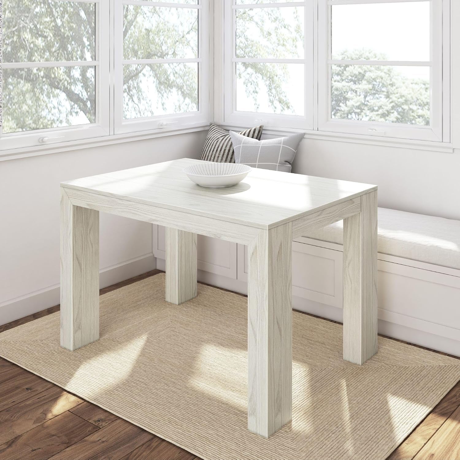 Square light‑wood table in a sunny corner seat area with a decorative bowl on the top.