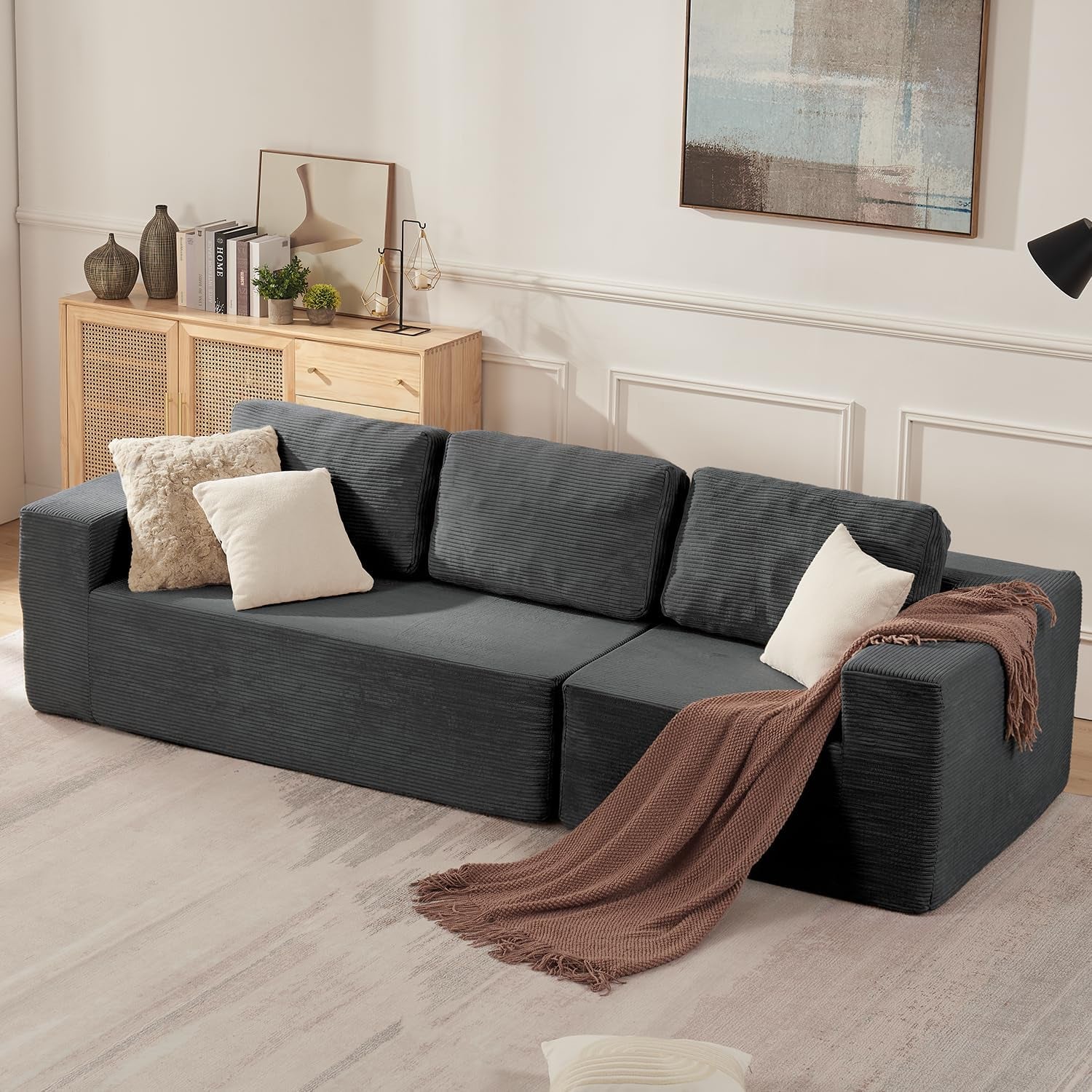 Dark gray corduroy-style modular sofa with three back cushions and a brown throw in a cozy room.