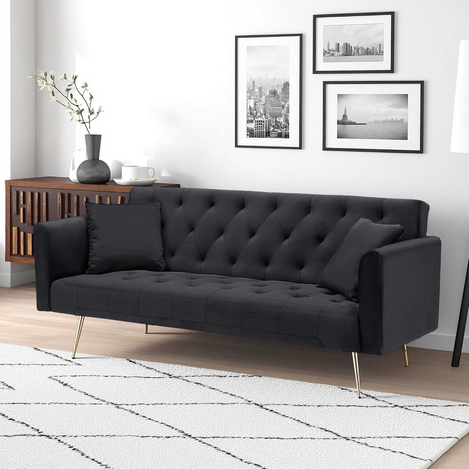 Angled front view of a dark charcoal velvet tufted sofa with gold legs beside a wooden console.