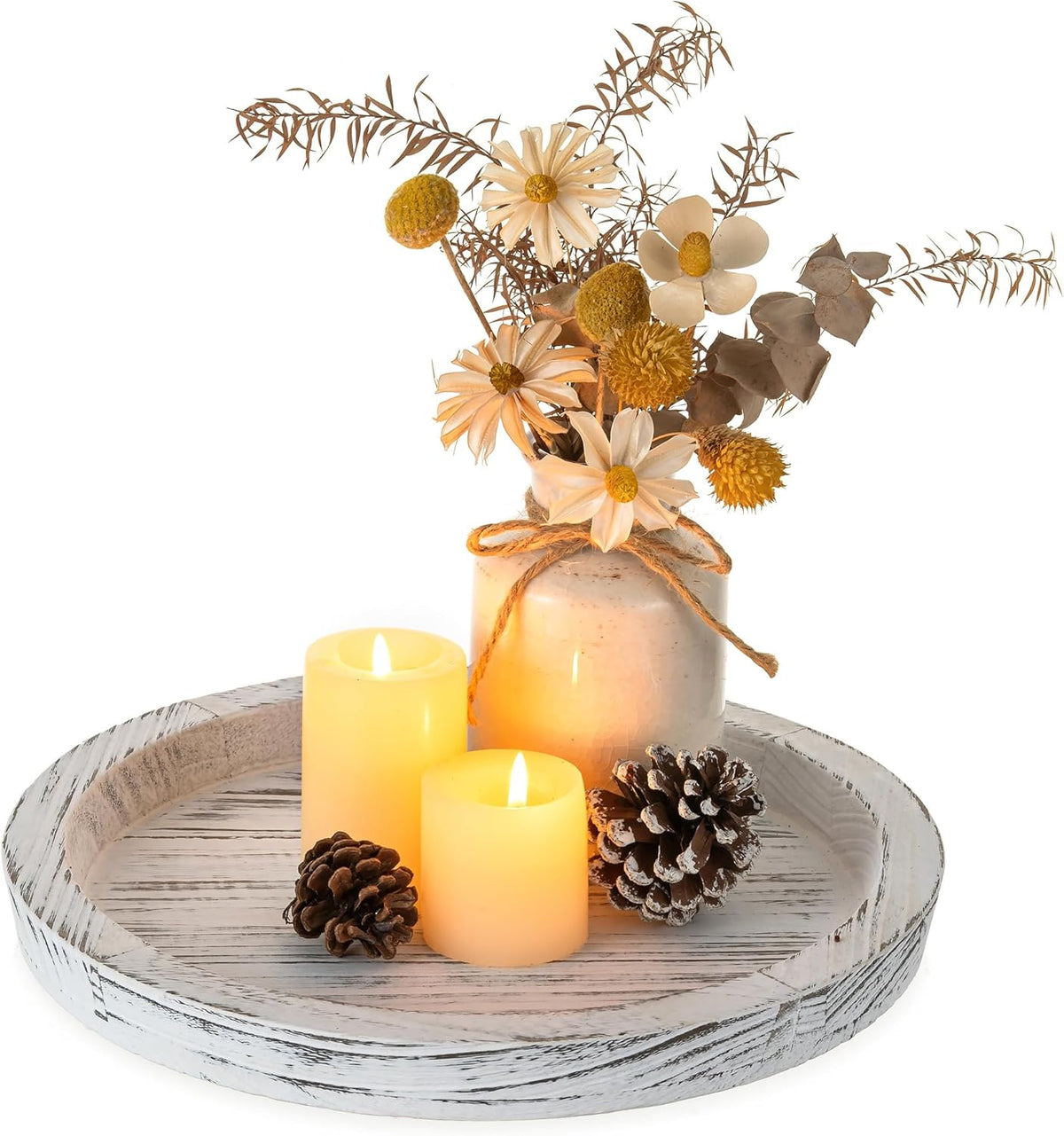 Whitewashed round tray styled with three glowing pillar candles, pinecones and a small floral vase.
