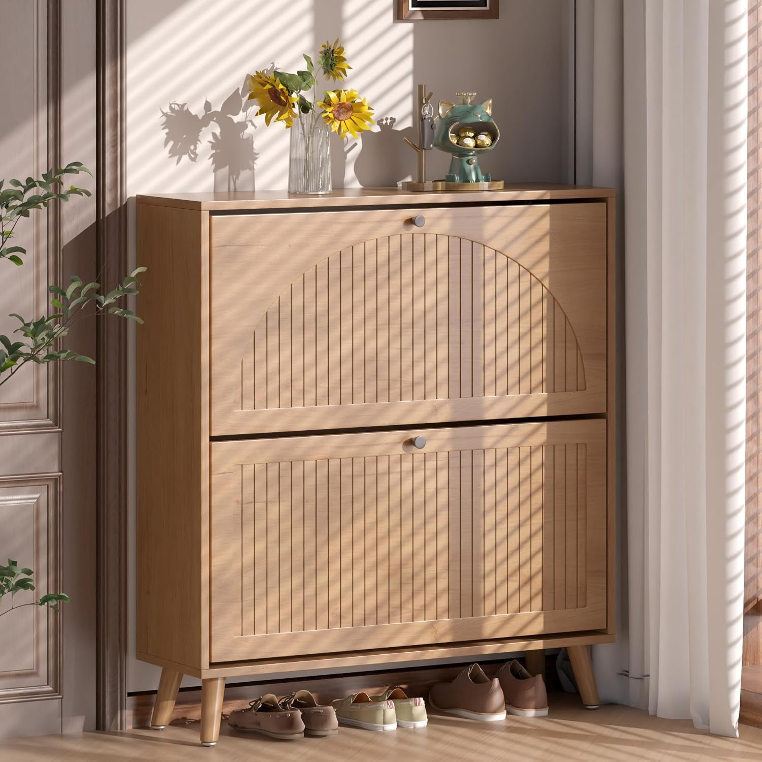 Natural wood two-drawer shoe cabinet with arched fluted front lit by window shadows