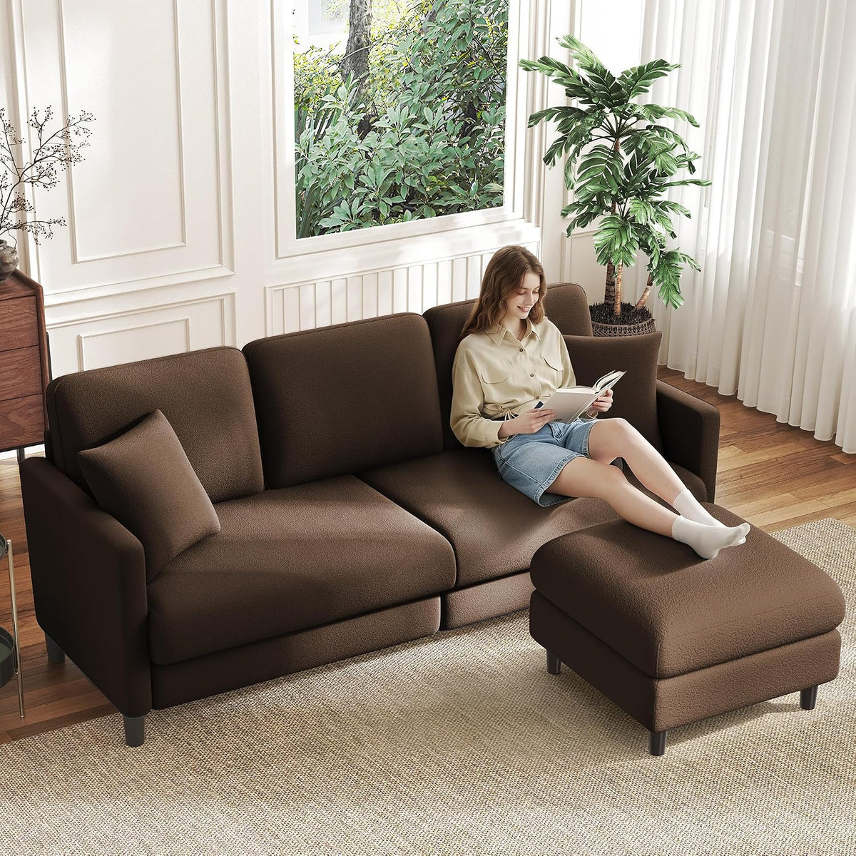 Brown loveseat with matching ottoman on a woven rug, woman reclining and reading a book.