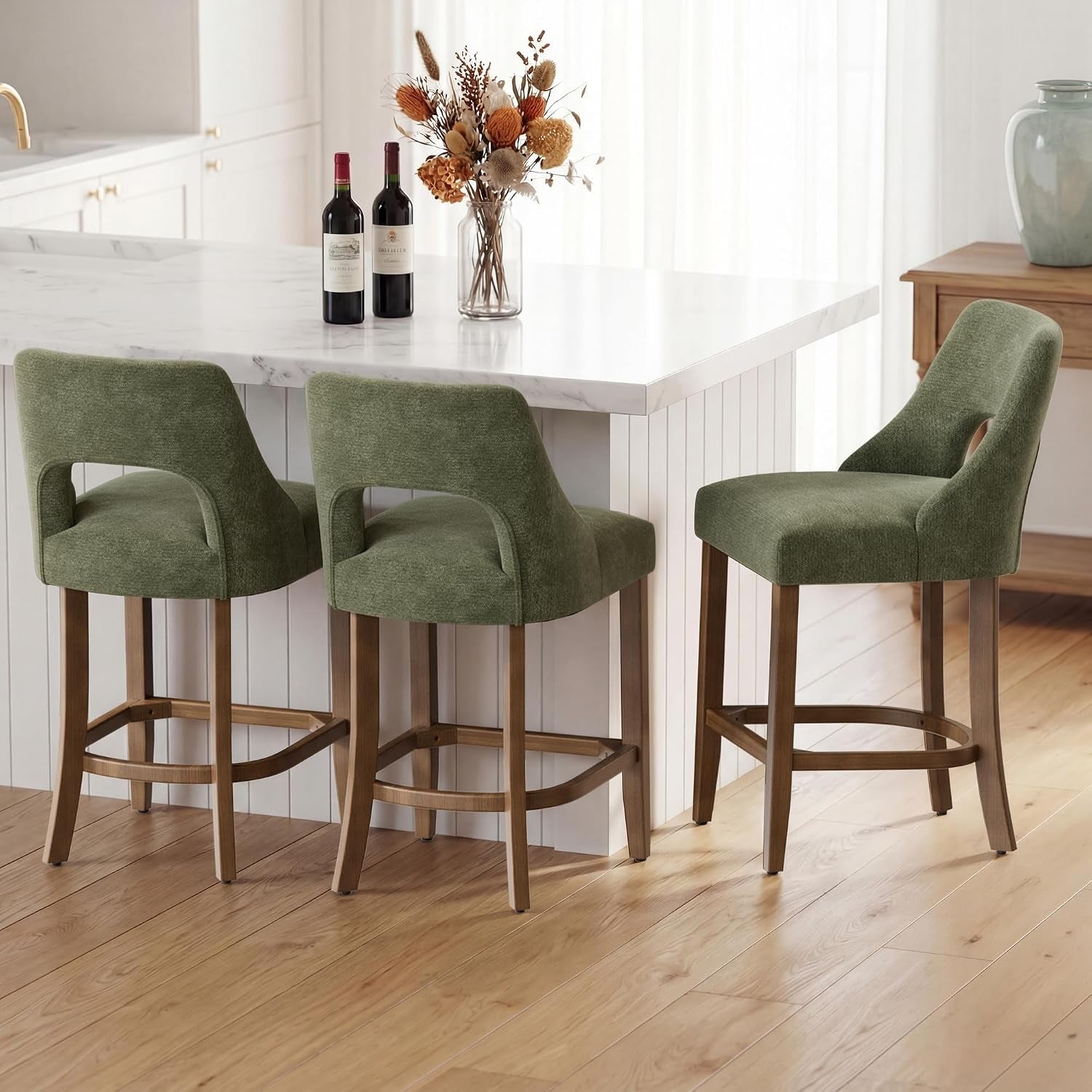 Three olive-green upholstered counter stools with wood legs arranged at a bright white island