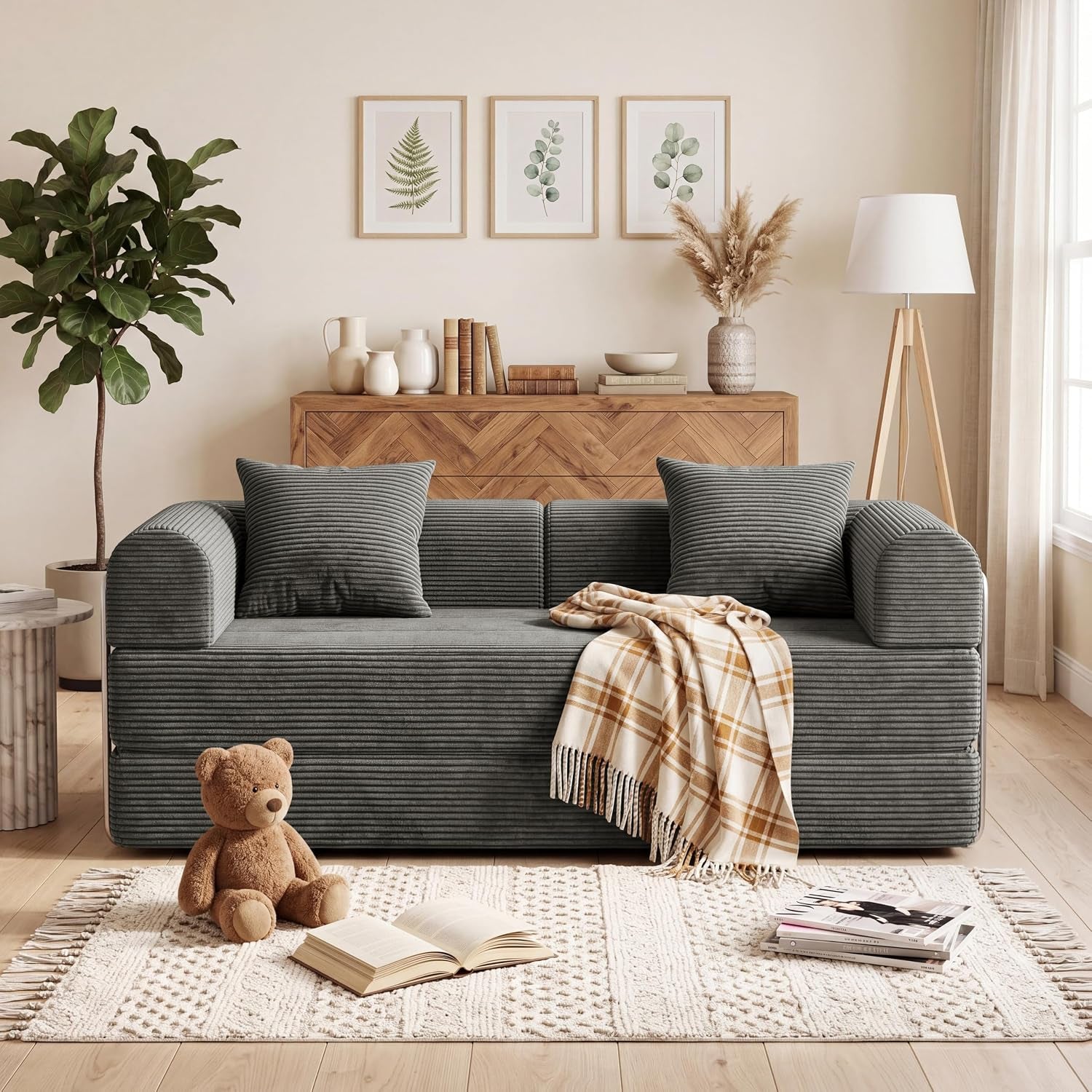 Gray corduroy futon sofa positioned against a wood console with a plaid throw and teddy on rug