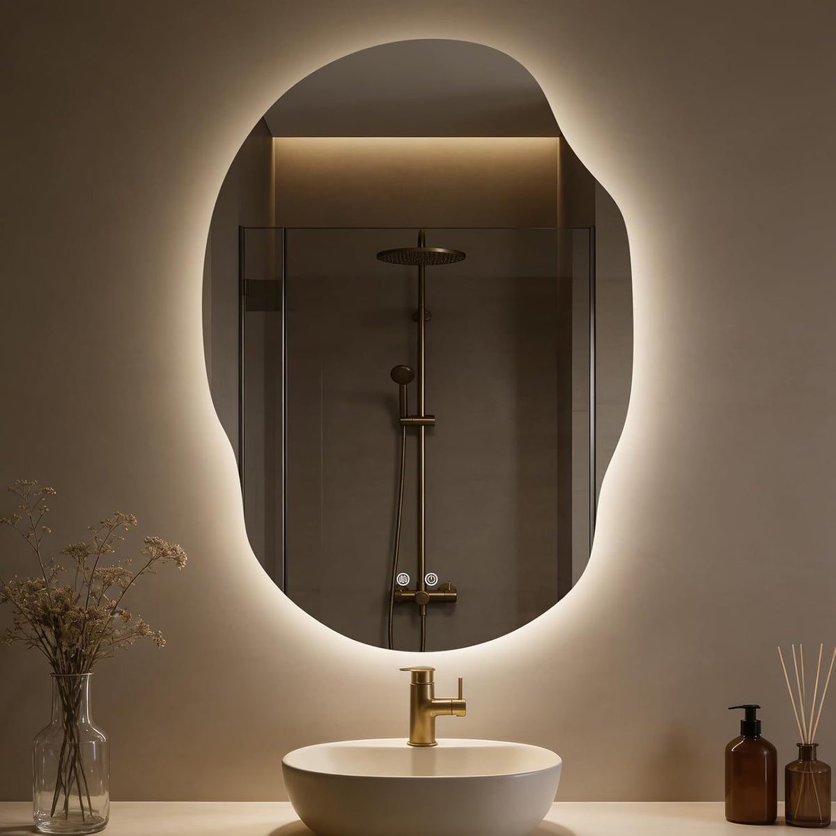 Irregular LED-backlit mirror reflecting a shower, shown over a sink with a single-handle gold faucet and glass vase with