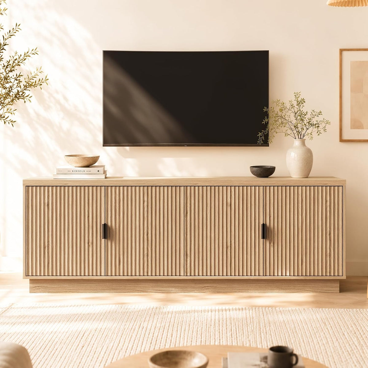 Light natural oak buffet with vertical fluted doors, vase and books on top, sunlight on wall.
