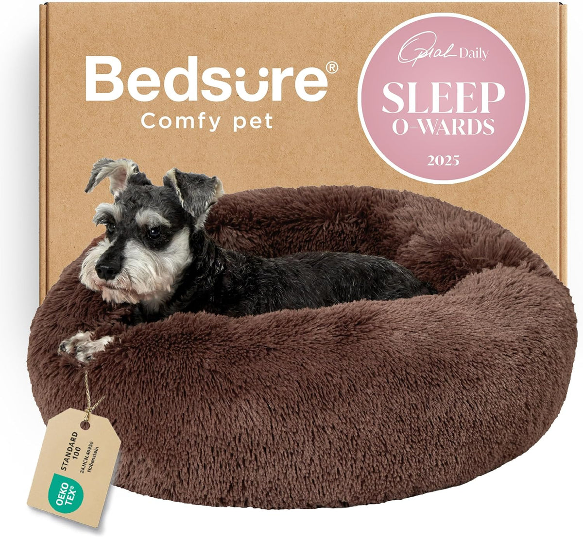 Cropped close-up of a small gray-and-white dog curled on a brown fluffy donut bed with a cardboard backdrop.