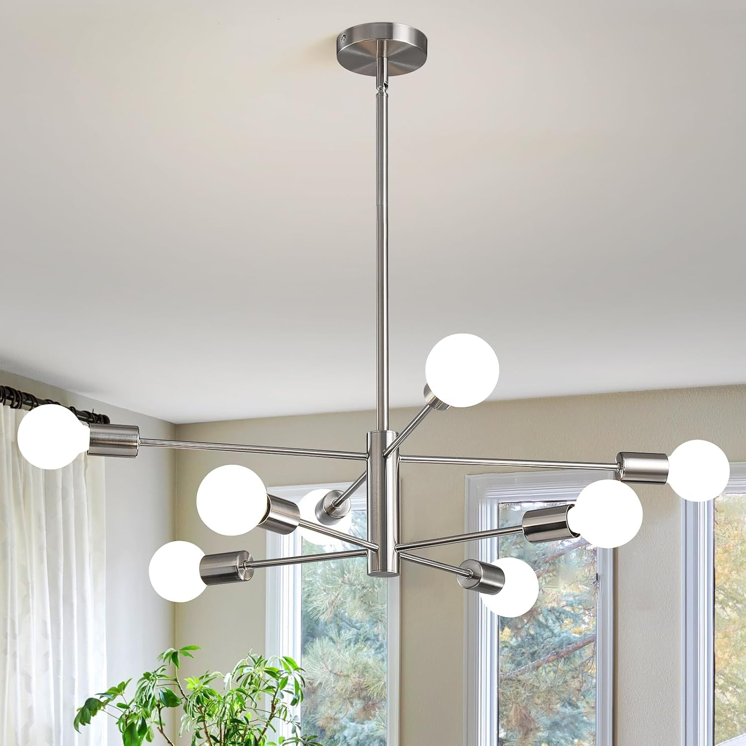 Close view of a silver sputnik chandelier suspended near tall windows and a potted plant.