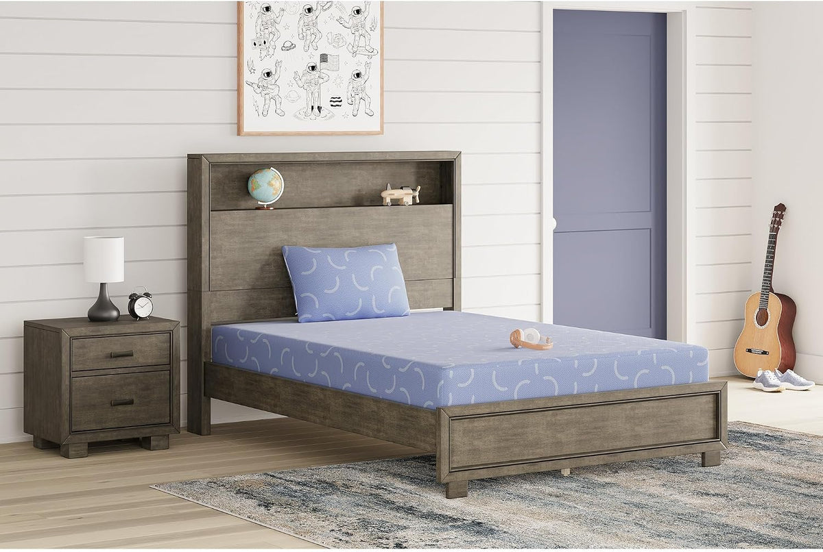 Blue patterned mattress and matching pillow on a gray wood bed with nightstand and guitar in a bright room.