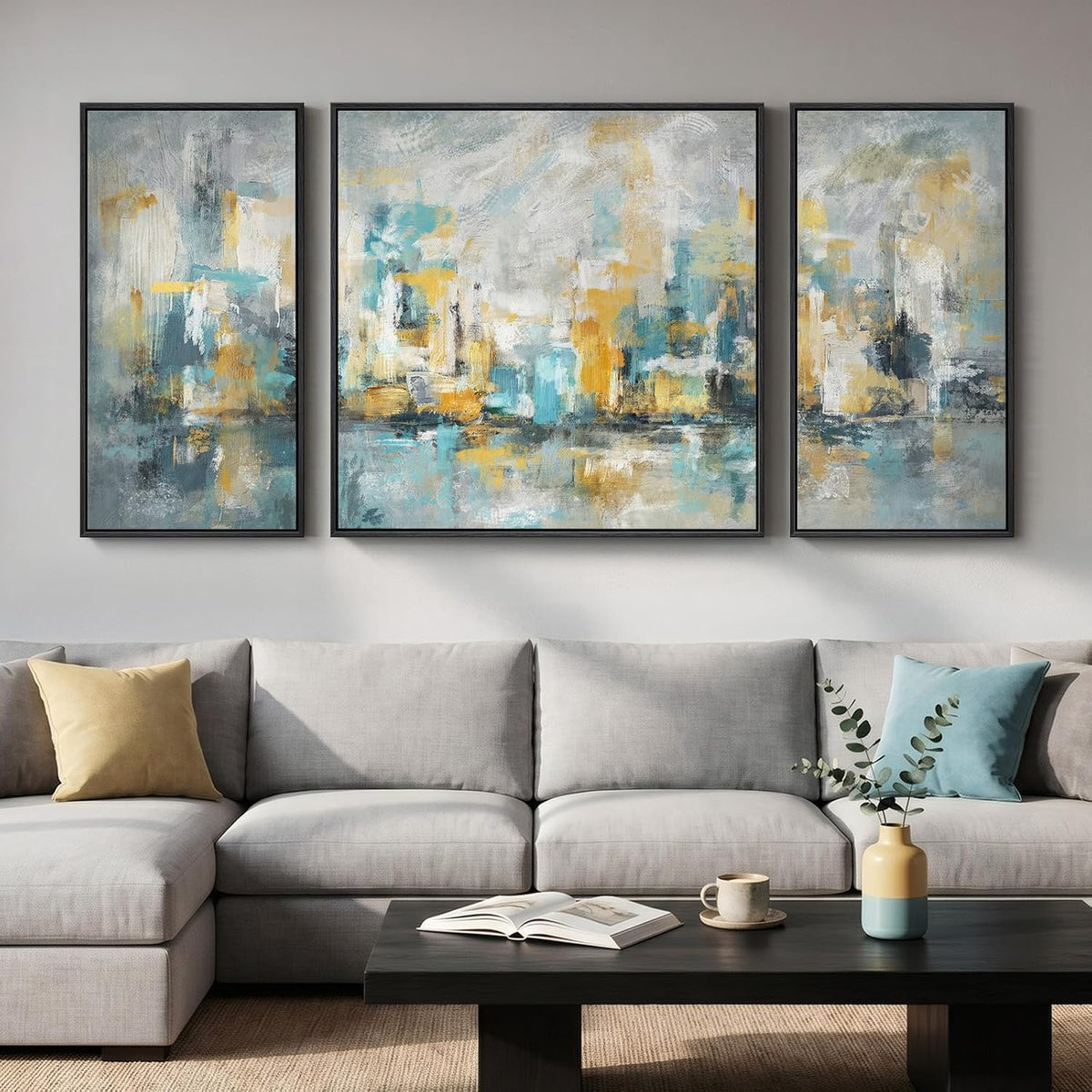 Three framed abstract panels in teal, blue and gold tones hung over a light gray sofa and dark coffee table.