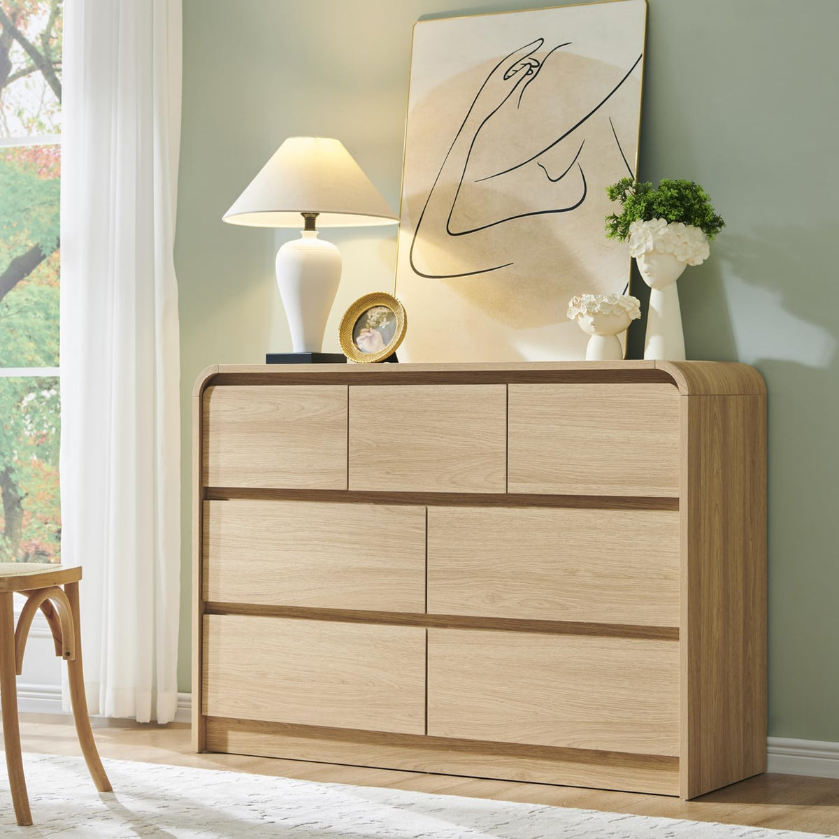 Low six-drawer dresser in a light oak finish topped with lamp and artwork against a pale green wall.