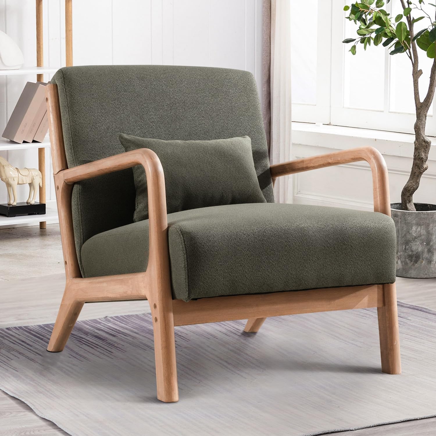 Olive-green upholstered armchair with curved light wood arms set on a rug by a window and plant.