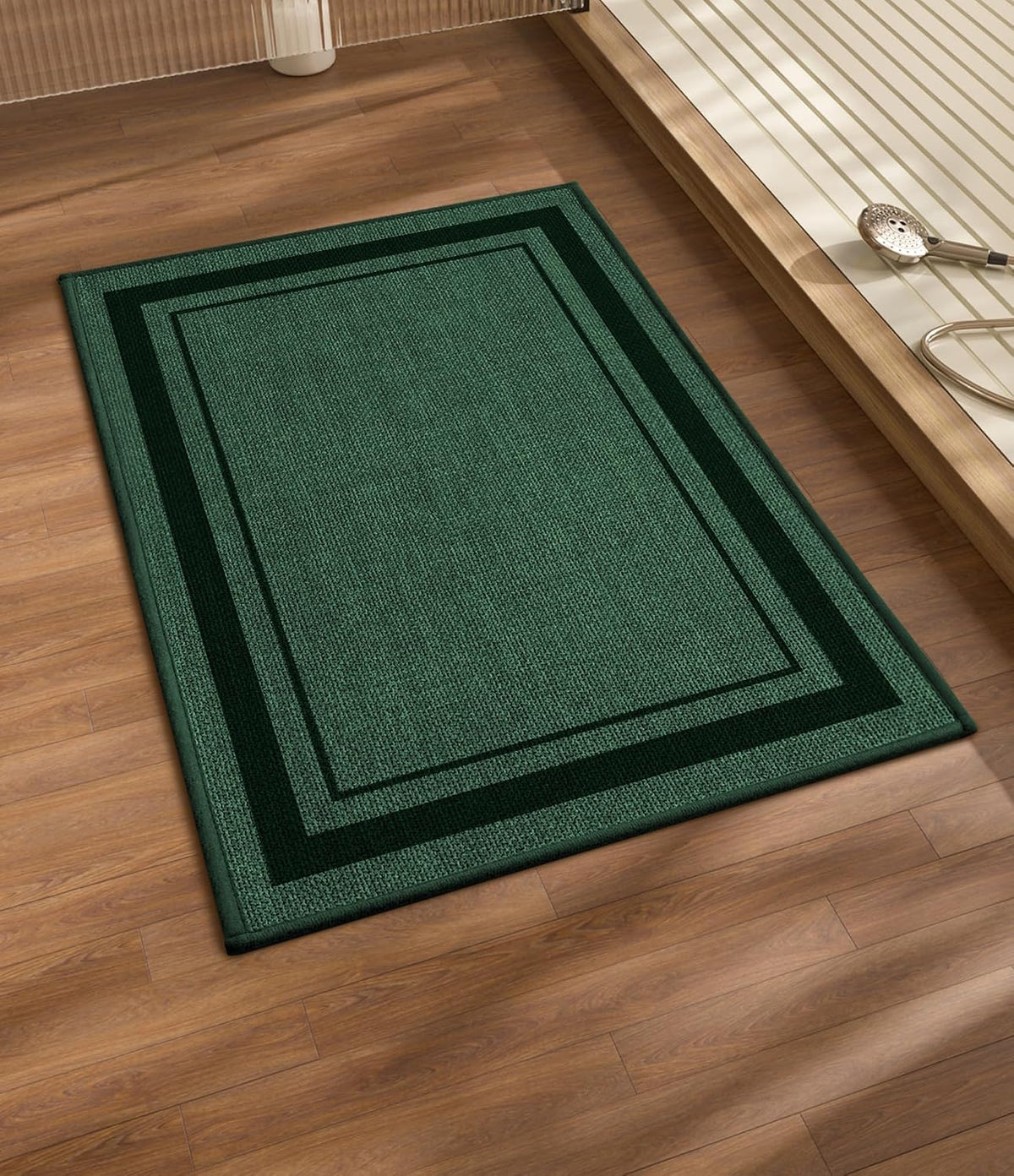 Dark green rectangular bath rug with double border laid on wood floor beside a tub