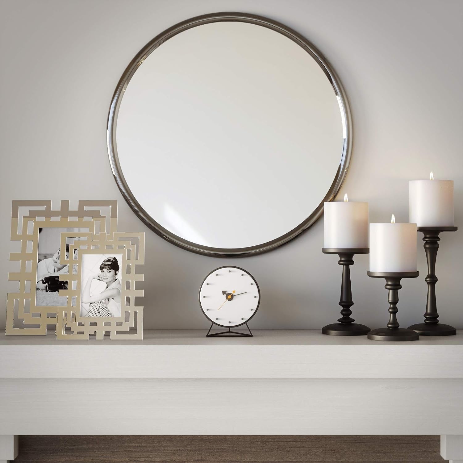 Three matte black candle holders staged on a mantel beneath a round mirror with photo frames