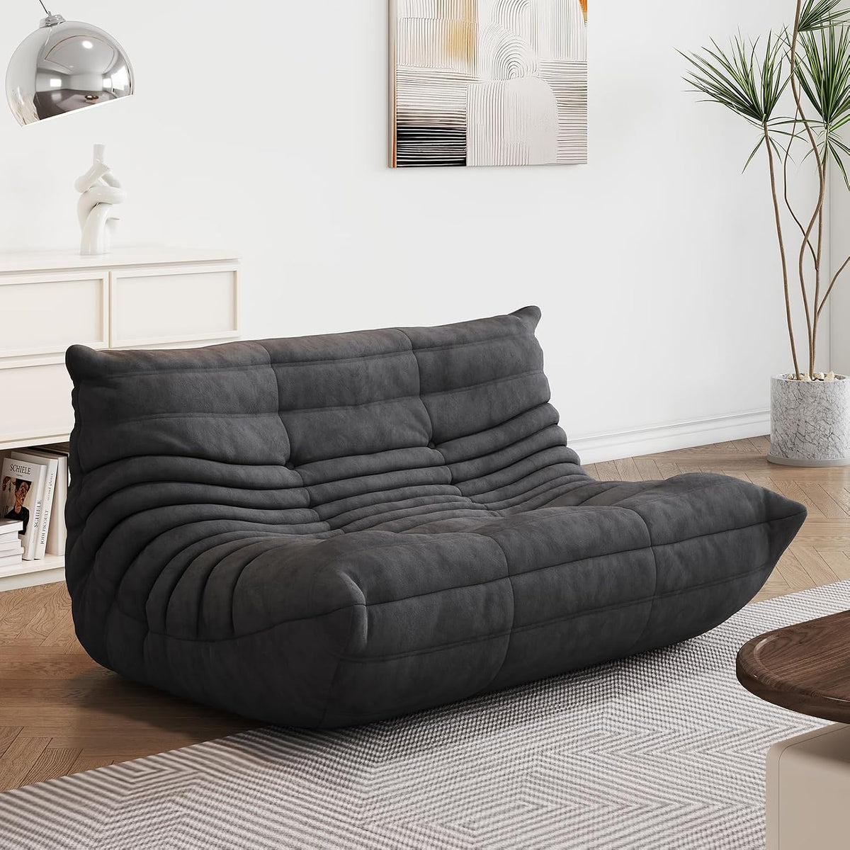 Charcoal two-seat bean bag loveseat in a living area with parquet floor and a potted plant at the wall.