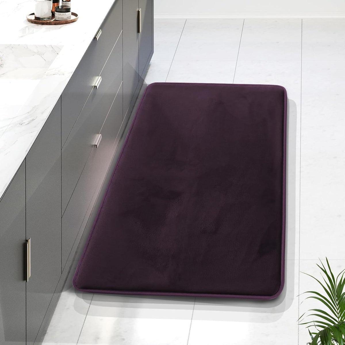 Long deep-purple rectangular bath rug placed alongside a gray bathroom cabinet on tile floor.