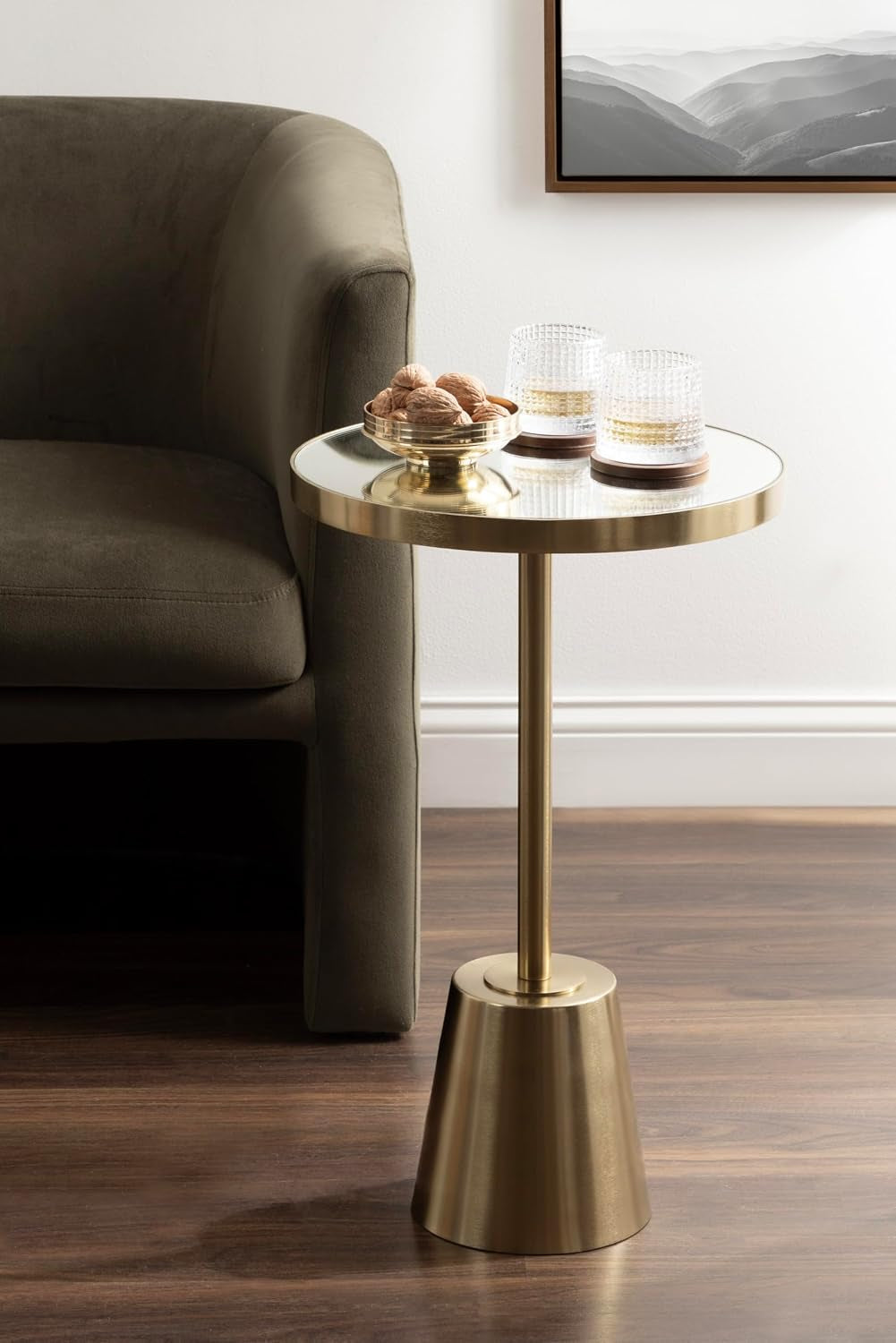 Gold mirrored side table staged beside an olive-green sofa on a wood floor with glass tumblers on top