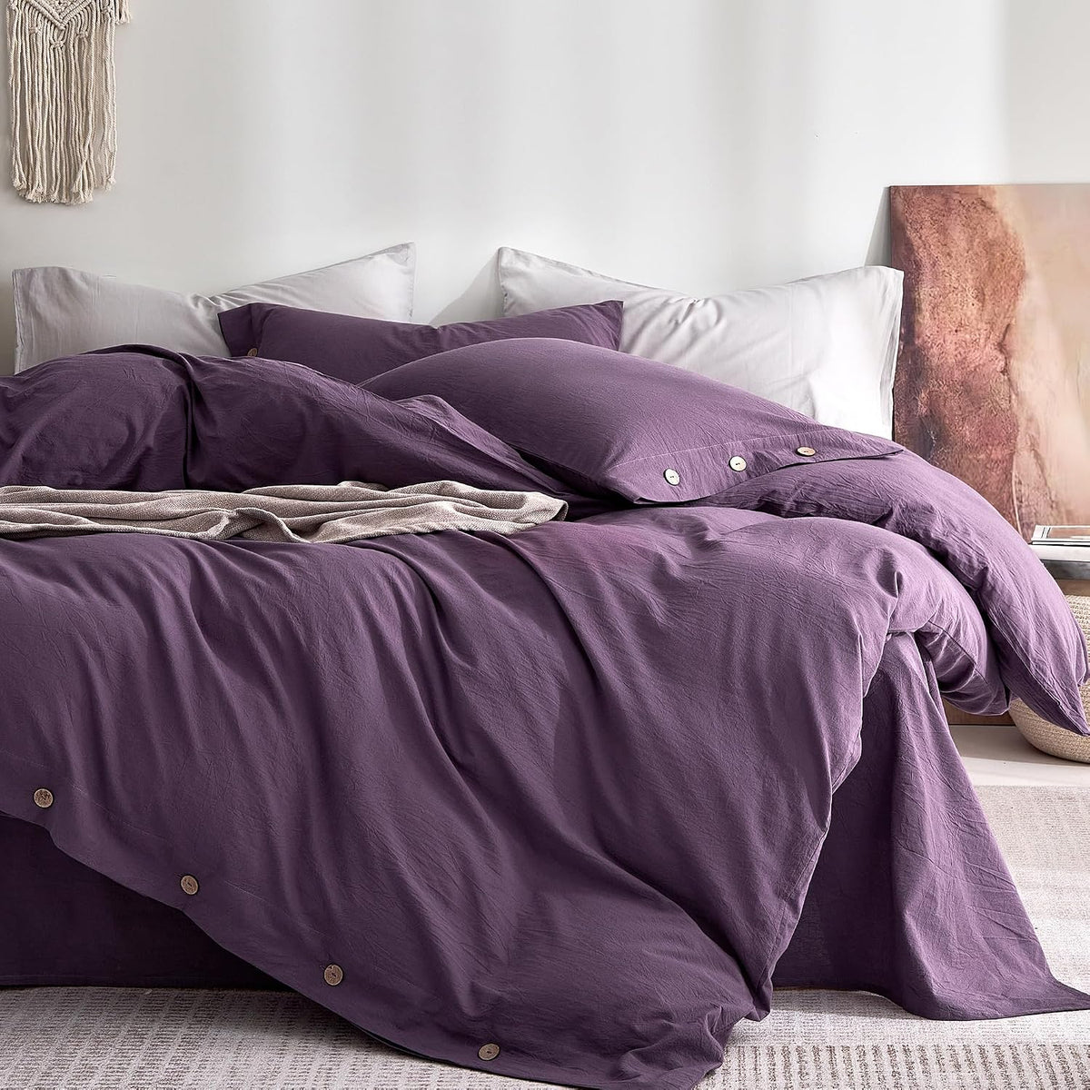 Bedroom scene showing a plum-colored duvet and pillows layered over pale shams with button closure.