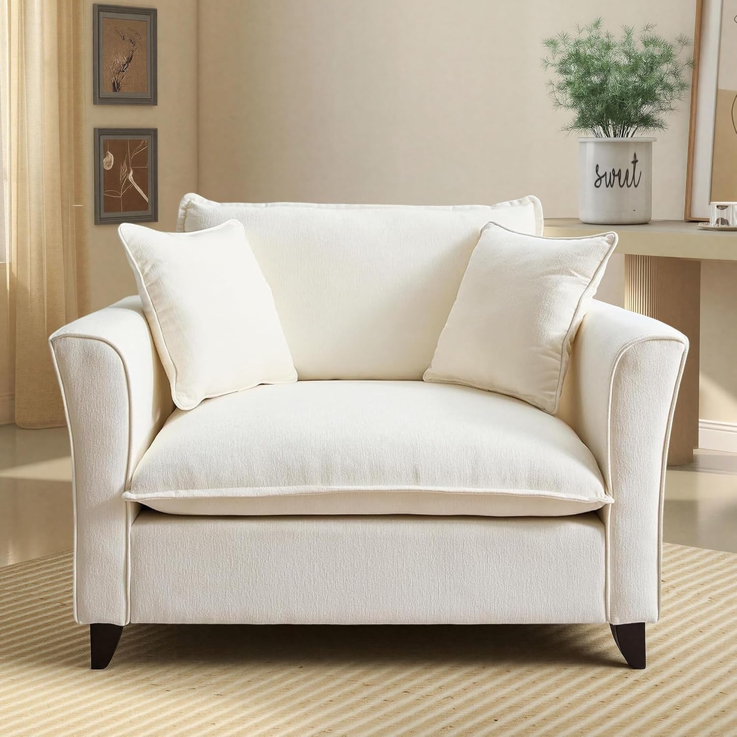 Straight-on front view of the oversized cream chair with two matching square pillows and flared armrests on a striped rug.