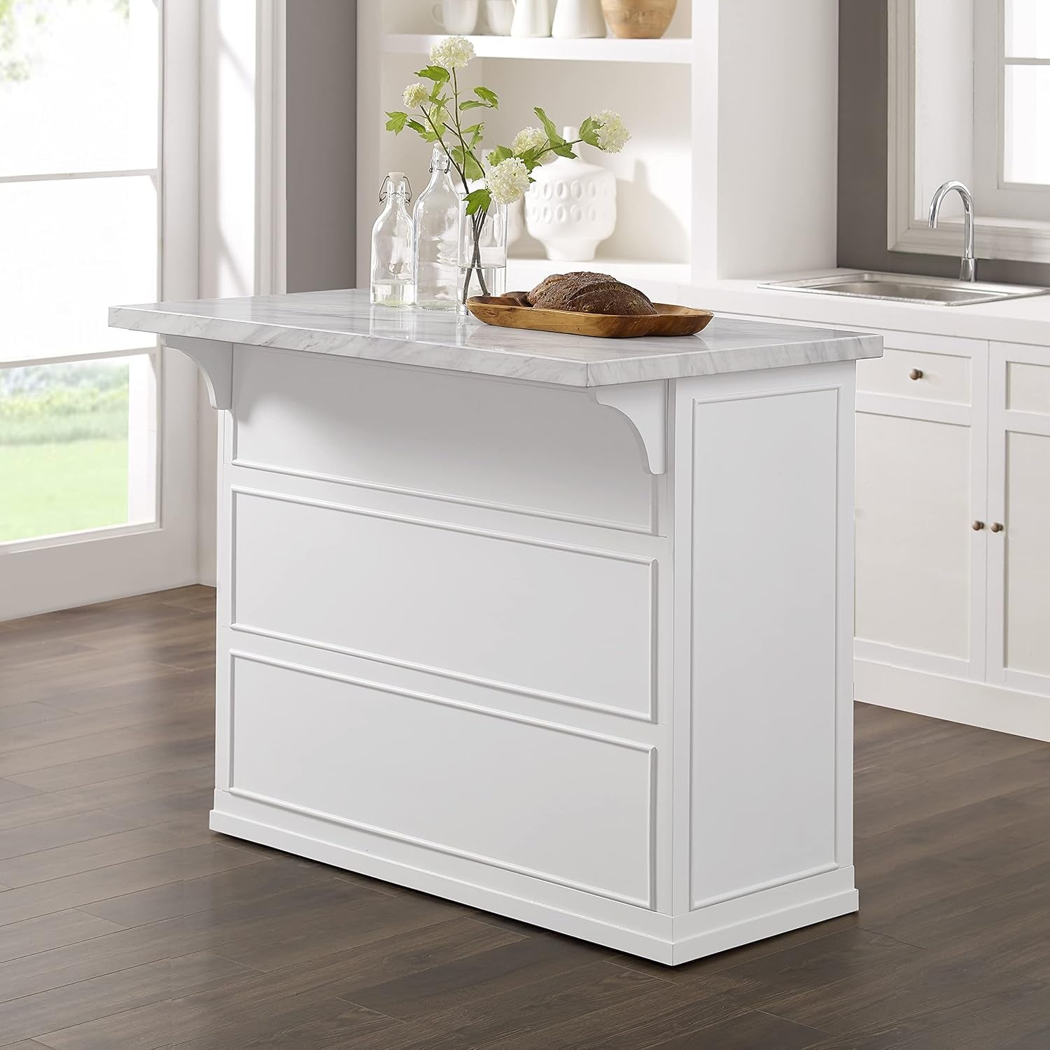 Angled rear shot showing the island’s stepped skirt and corbel-style support under the overhang with a sink in the background