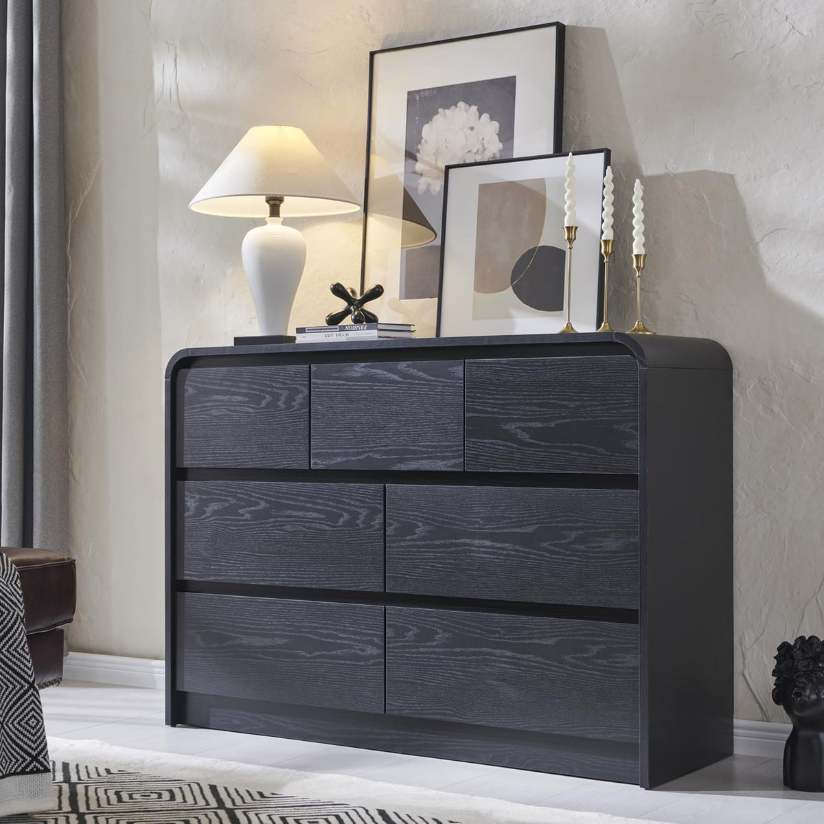 Matte black six-drawer dresser staged with lamp, candles and framed prints against a textured wall