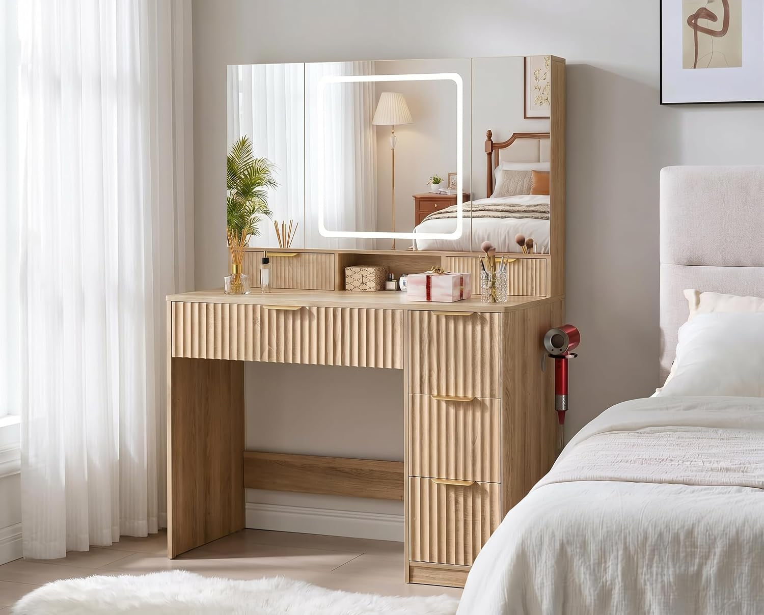 Fluted wood-finish vanity desk with central LED mirror, staged beside a bed in a bedroom