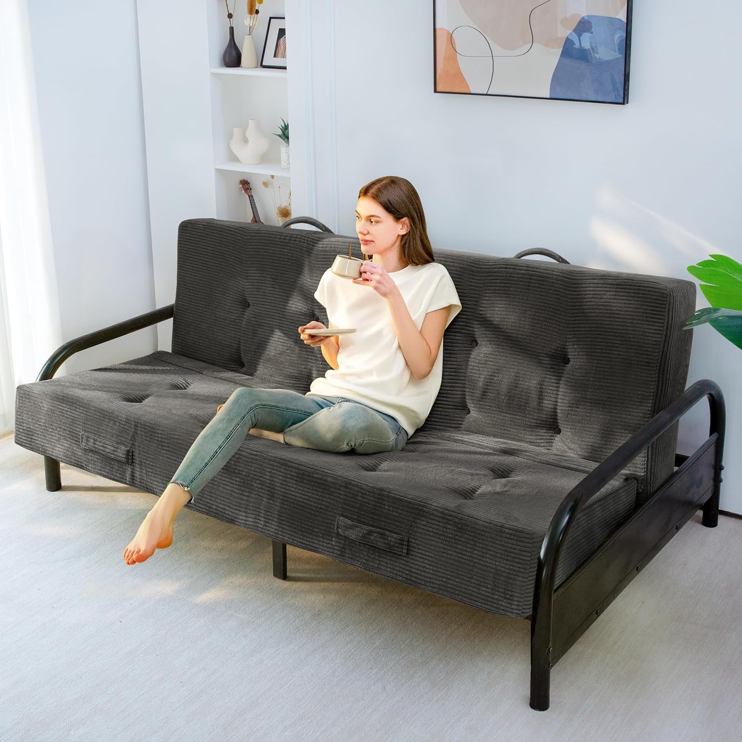 Woman relaxing on a dark gray corded futon mattress with handles, placed on a black metal futon frame.