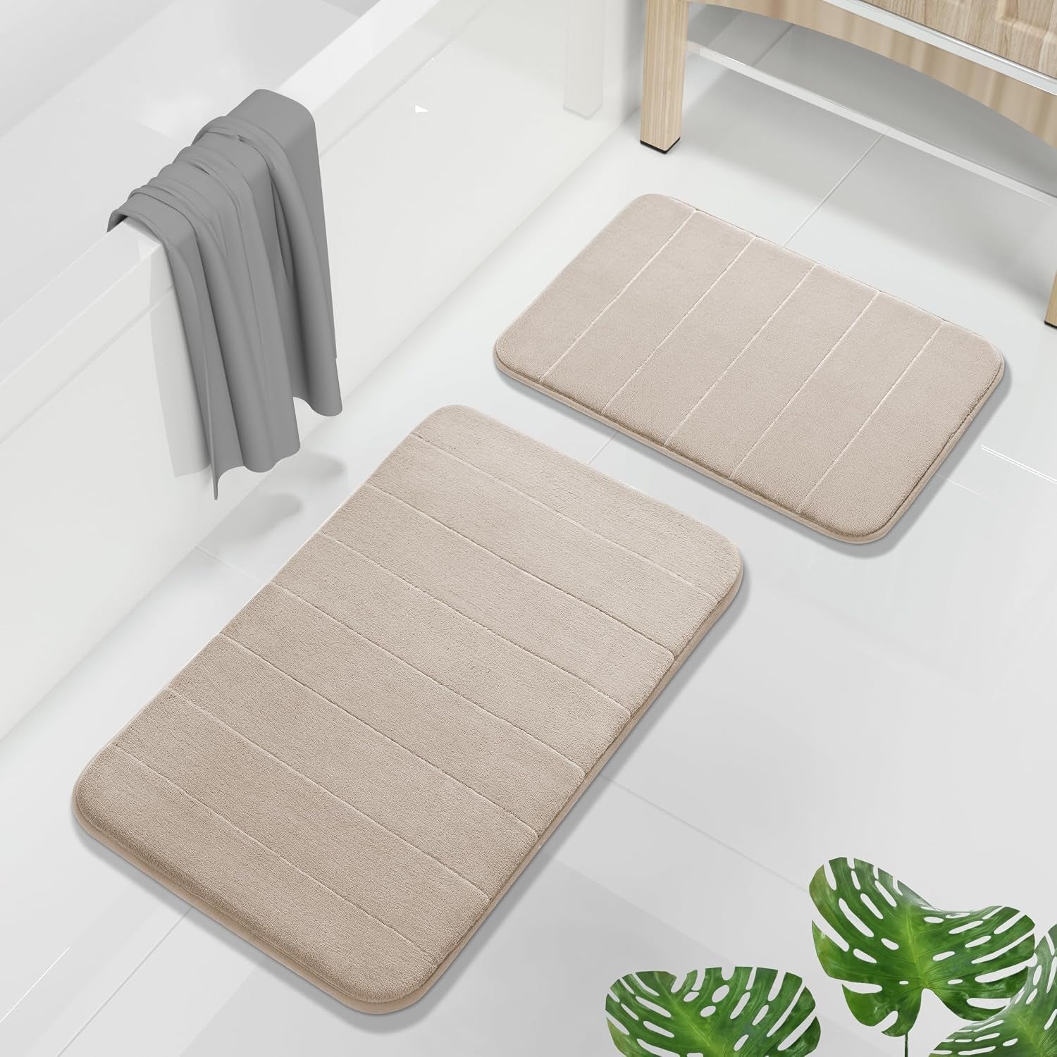 Beige memory foam large and small rugs placed on white bathroom tile beside a bathtub, top-down view