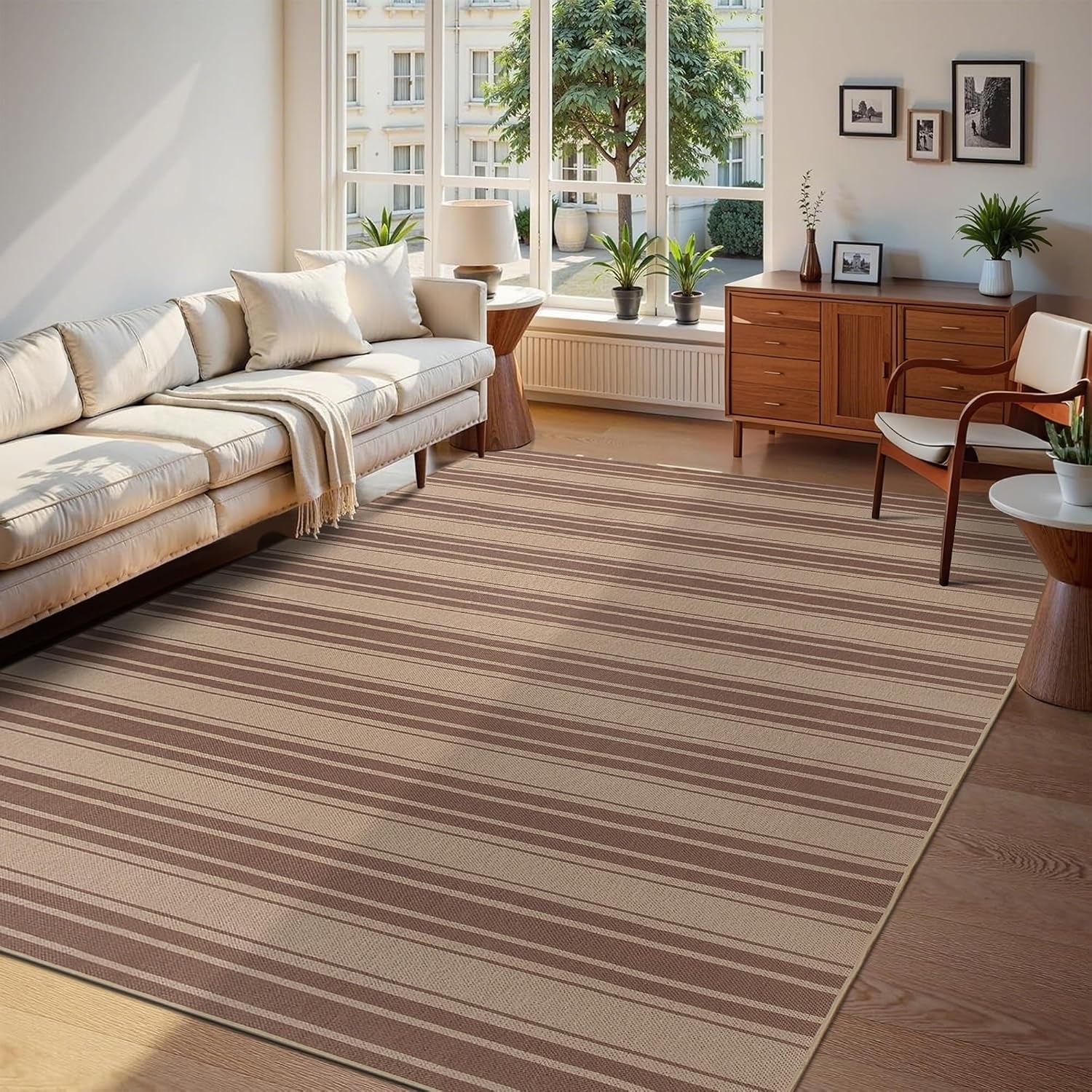 Low-angle view of a striped taupe rug under a light sofa and wooden sideboard by tall windows