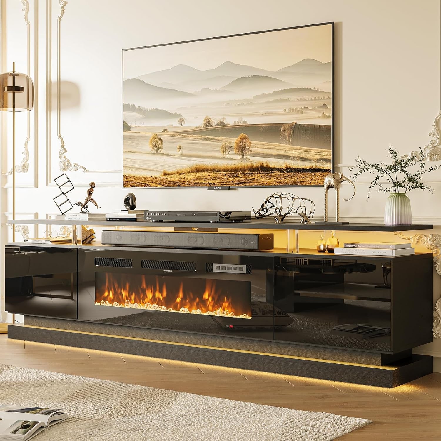 Front view of black high-gloss console with warm fireplace glow beneath a wall-mounted television in a bright room
