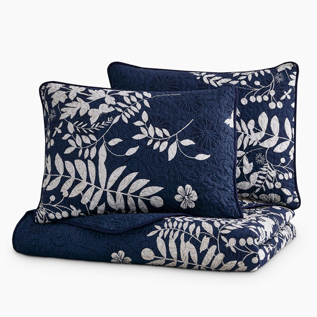 Two rectangular navy pillow shams propped behind a folded navy quilt, showing piped edges and matching print