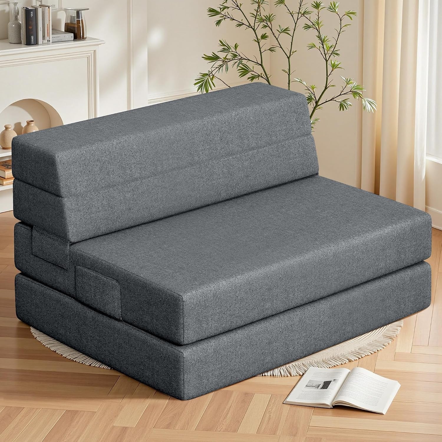 Dark gray folding sofa set up as a low couch in a living room beside a rug and plant.