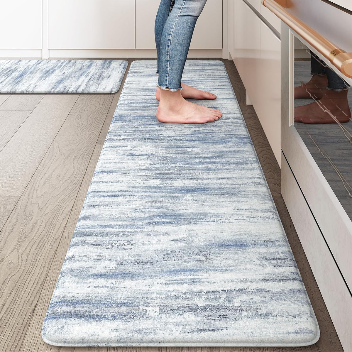 Bare feet standing on a long blue-gray abstract runner next to lower cabinets and oven.