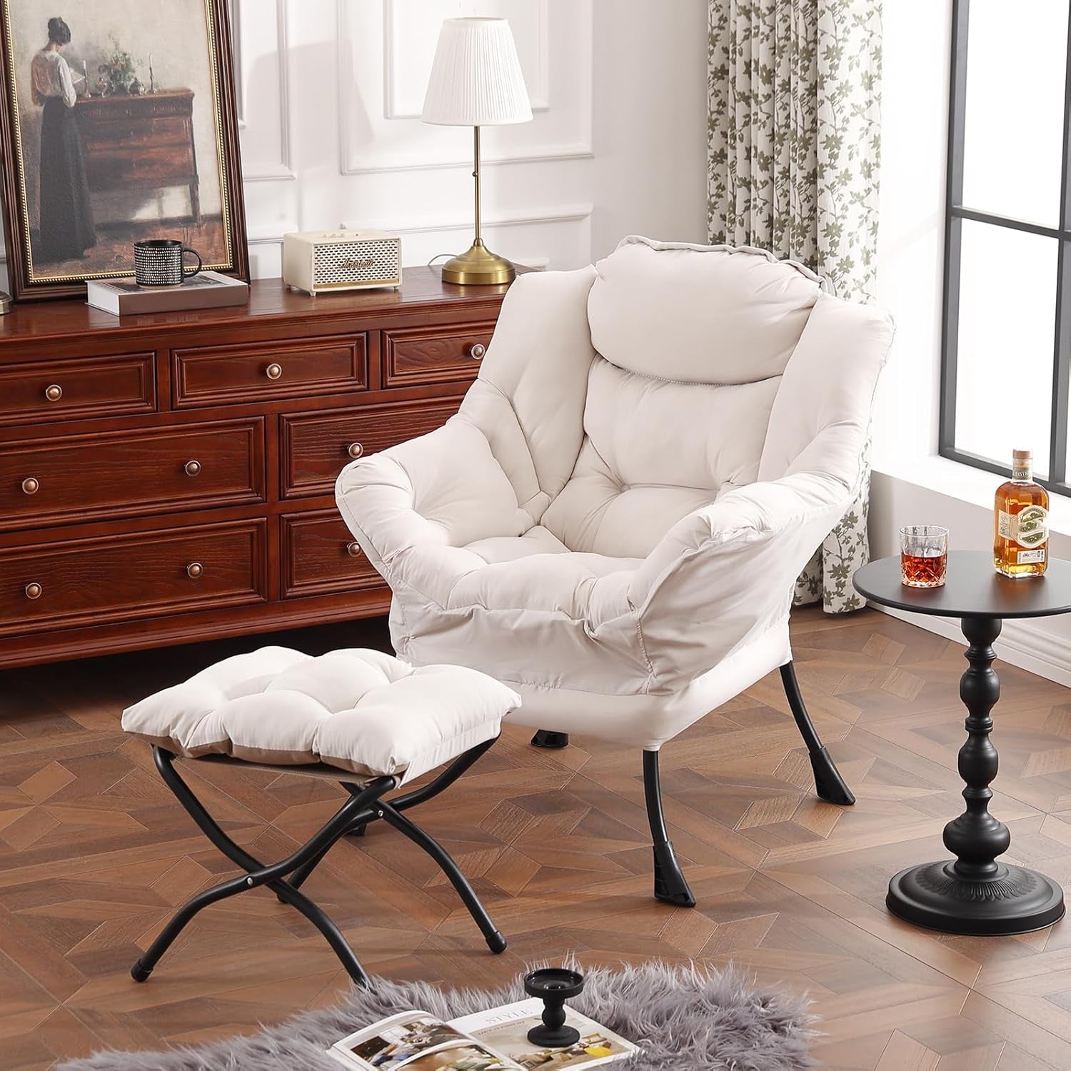Cream upholstered lounge chair with matching ottoman beside a wooden dresser and side table in a bright room