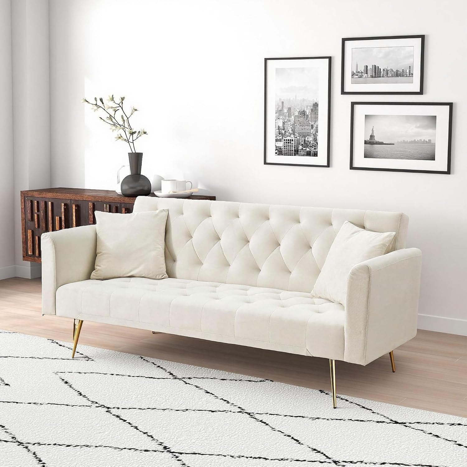 Angled view of a cream velvet tufted sofa with gold legs beside a wooden console and framed wall art.