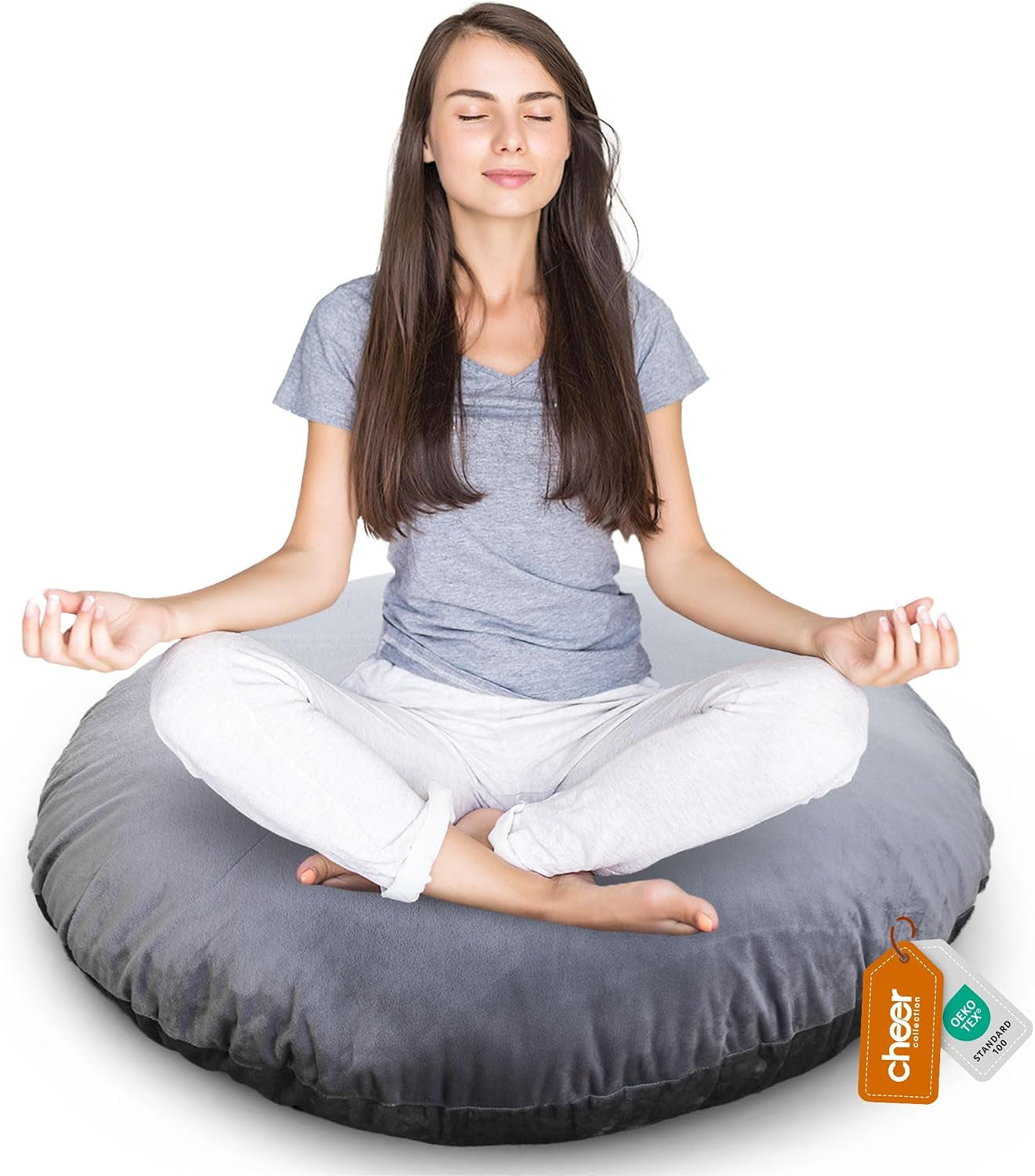 Woman seated cross-legged on a light gray round floor pillow, relaxed pose on a white background.