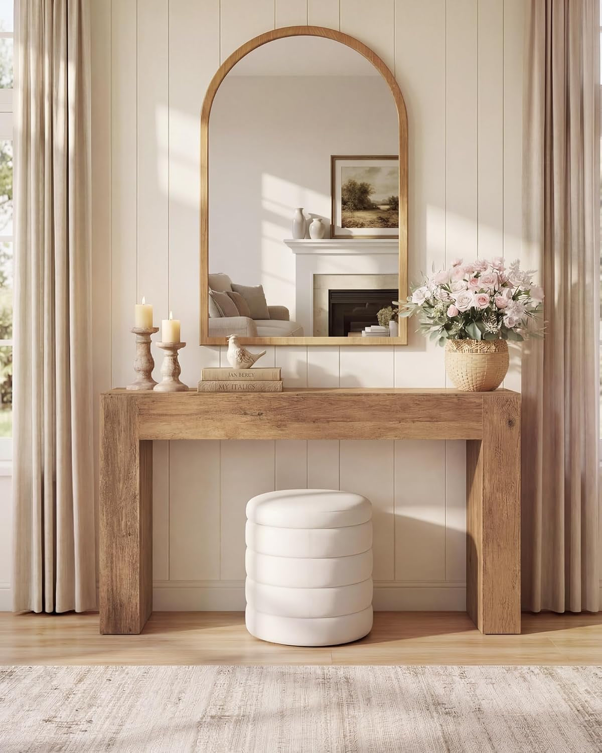 Console table used as a vanity beneath a large arched mirror with a round white pouf and decorative candles