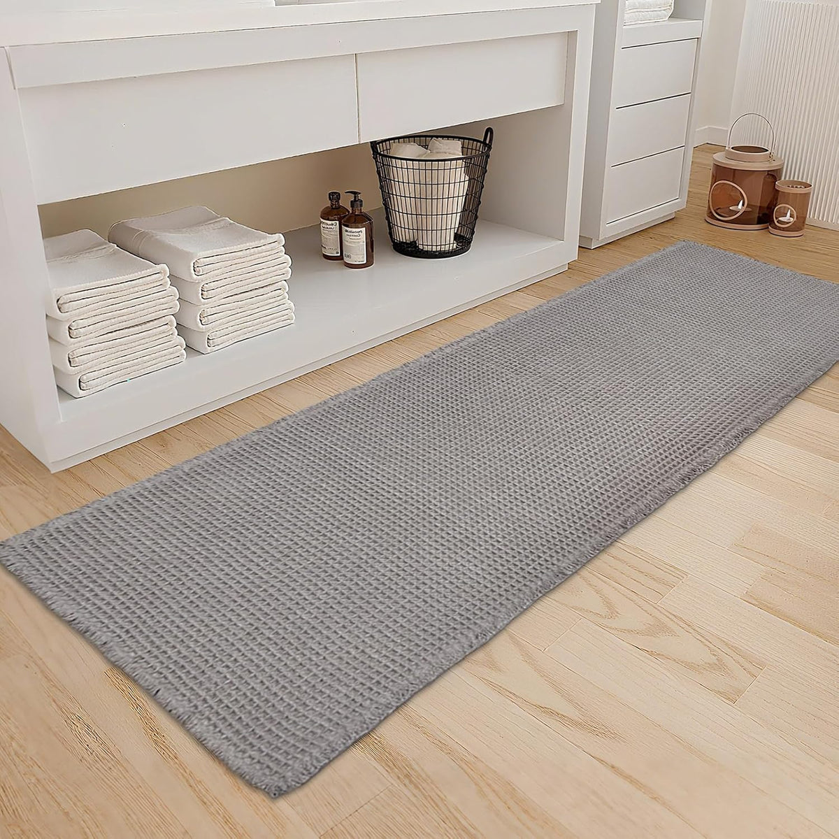 Light gray waffle runner rug laid in front of a white vanity on a wood floor.
