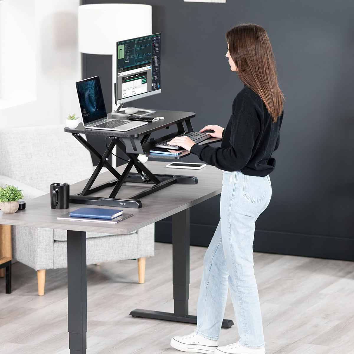 Person using a black standing desk converter on a desk with monitor and laptop
