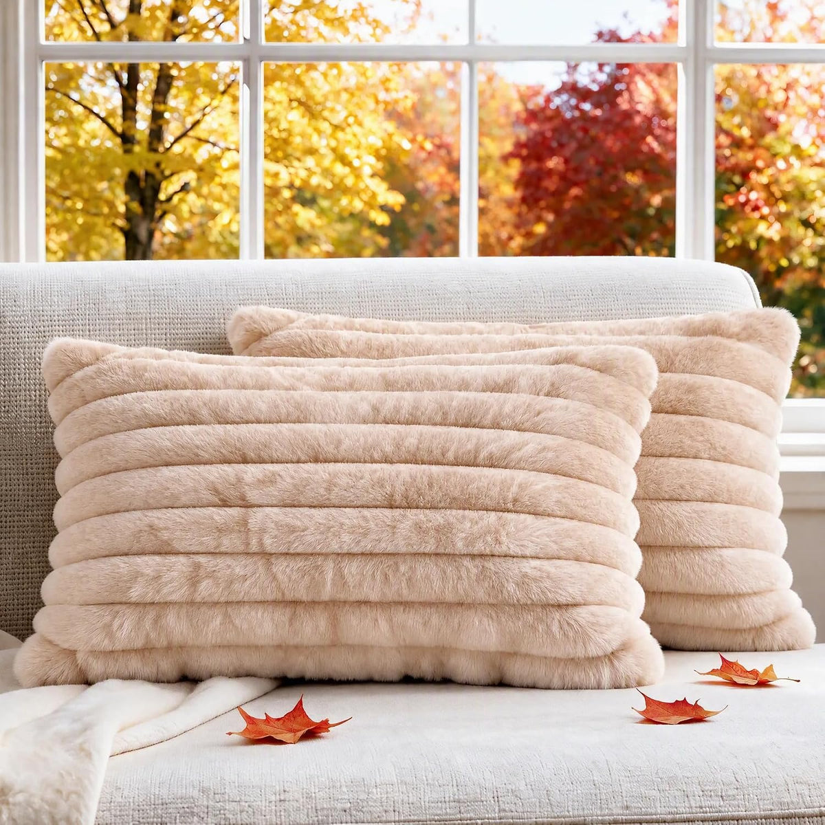 Two light beige faux fur ribbed pillow covers on a textured sofa seat with scattered autumn leaves