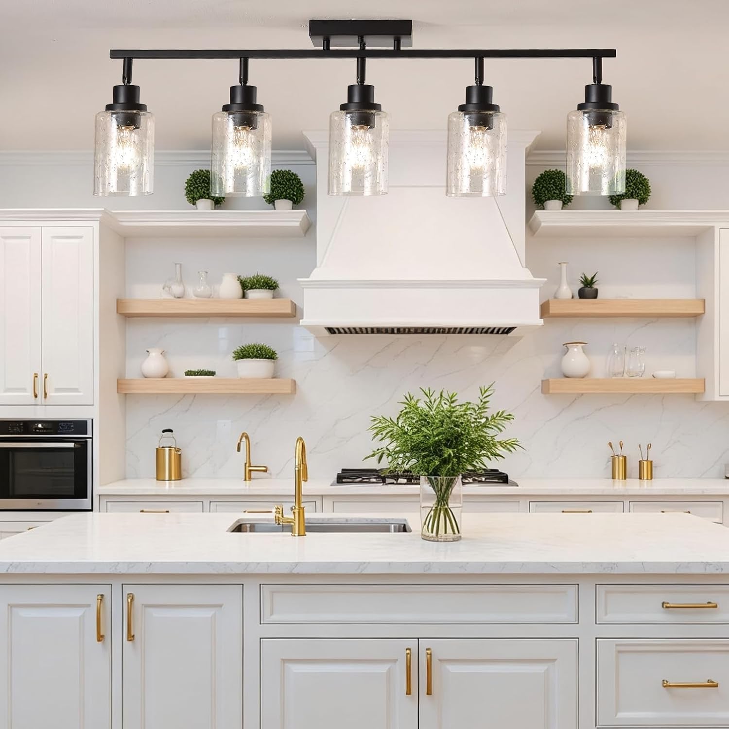Matte black five-light track centered over a white kitchen island with gold faucet and open wood shelves.