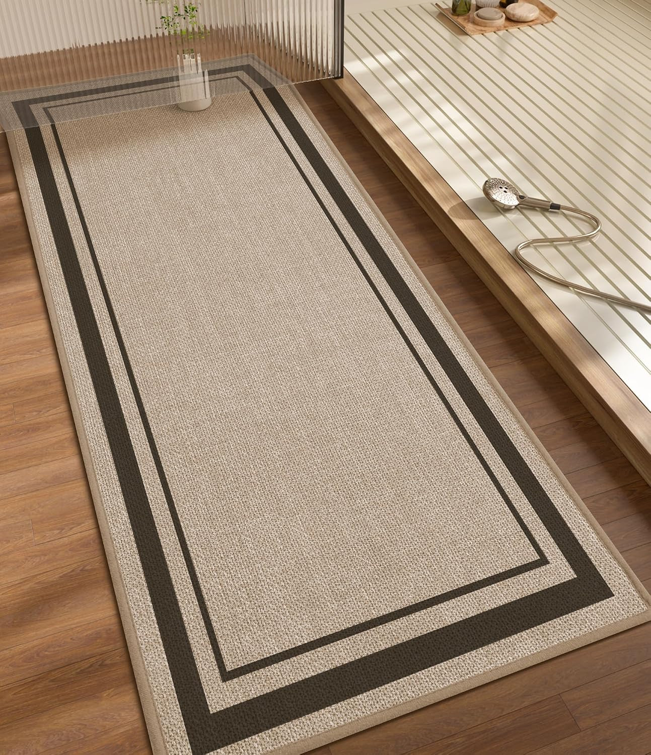 Long rectangular beige runner with double dark border on wood floor beside a sunken shower