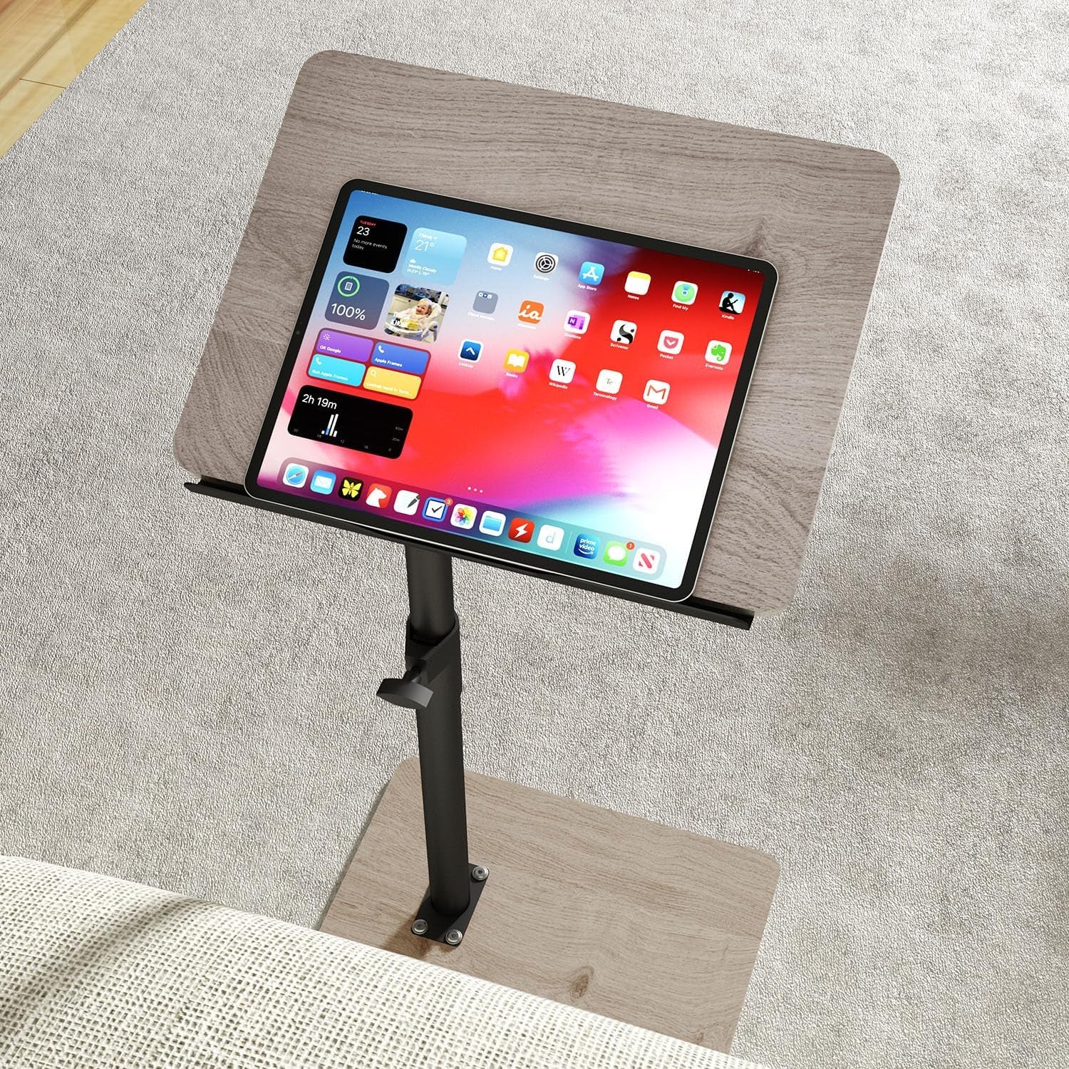 Light gray wood tray table with black pole over carpet holding a tablet on the surface