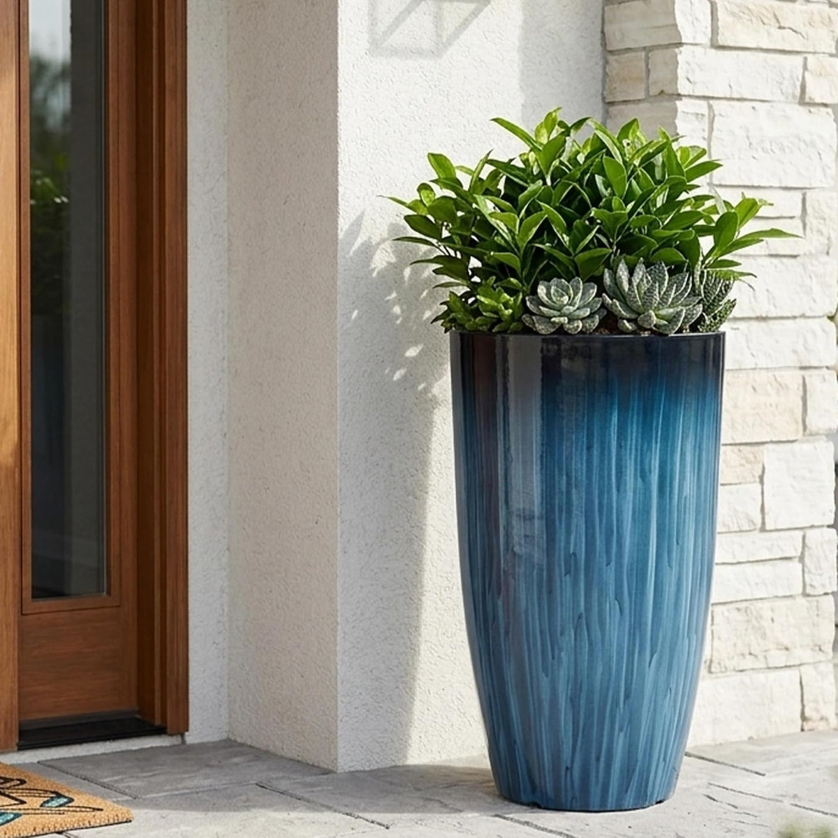 Tall blue gradient planter placed on a front porch beside a wood-trimmed door, filled with greenery