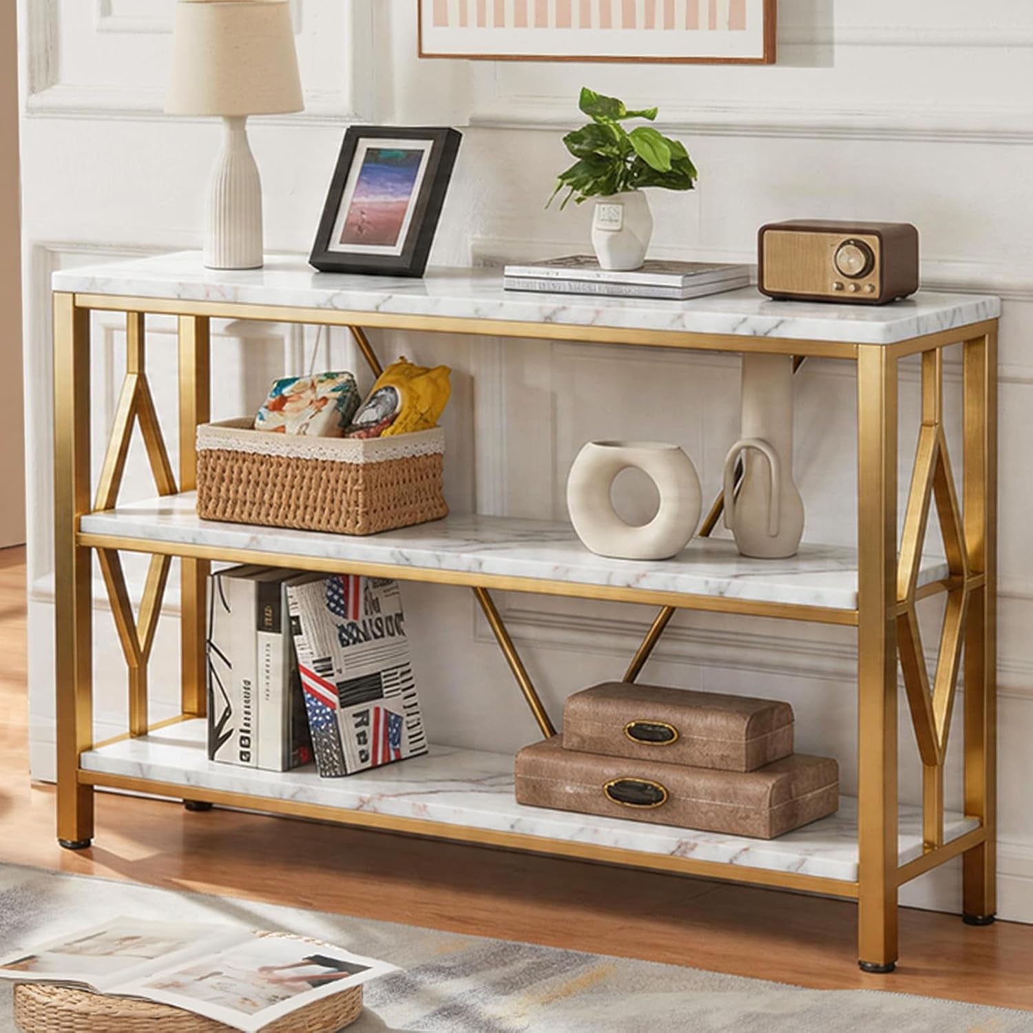 Side-front view of a gold‑frame console table with white marble-look shelves styled with decor.