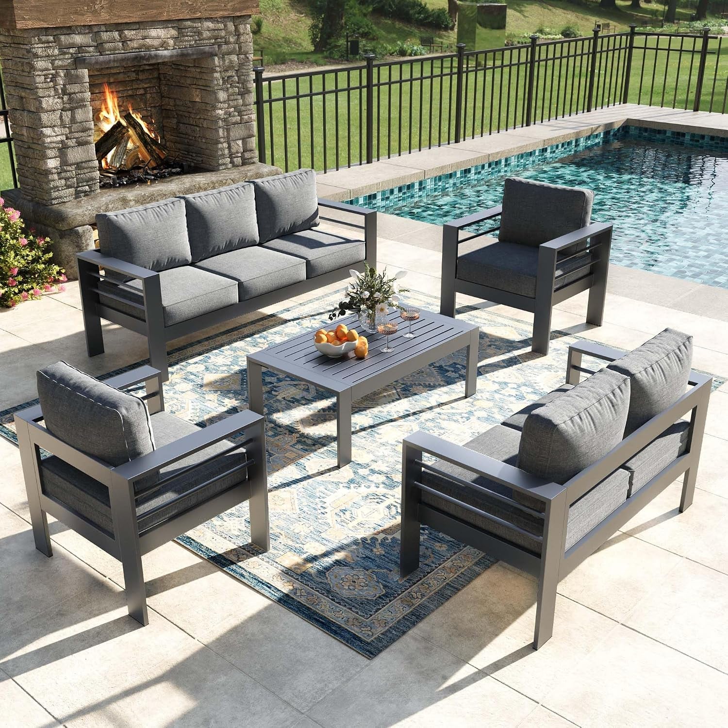 Outdoor patio conversation set: two three-seat sofas, two armchairs, rectangular coffee table on patterned rug by pool and