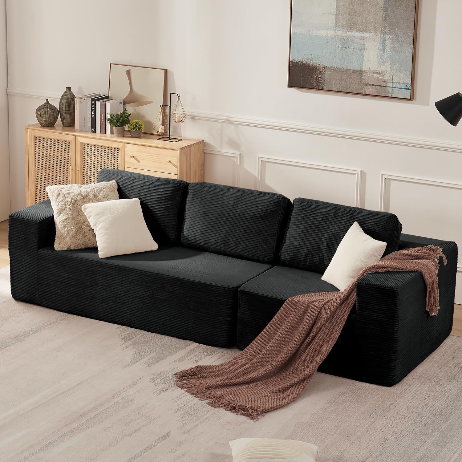 Low black modular L‑shaped sofa with three back cushions, throw blanket and pillows in a living room with light wood
