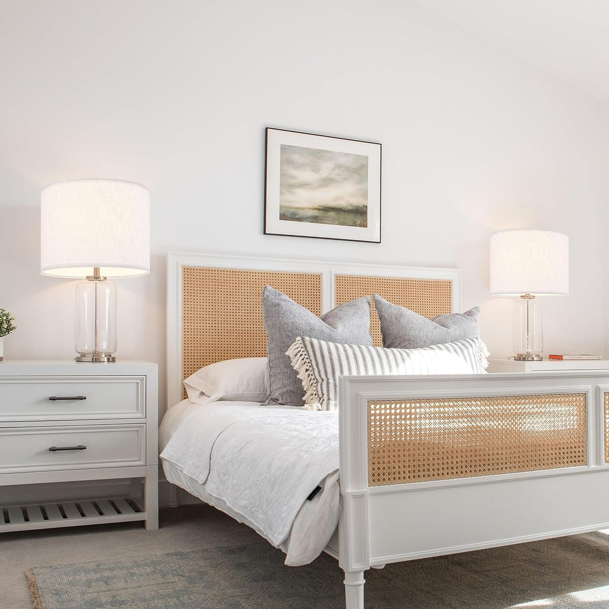 Bedroom scene with two natural linen drum lampshades on bedside table lamps flanking a white bed.
