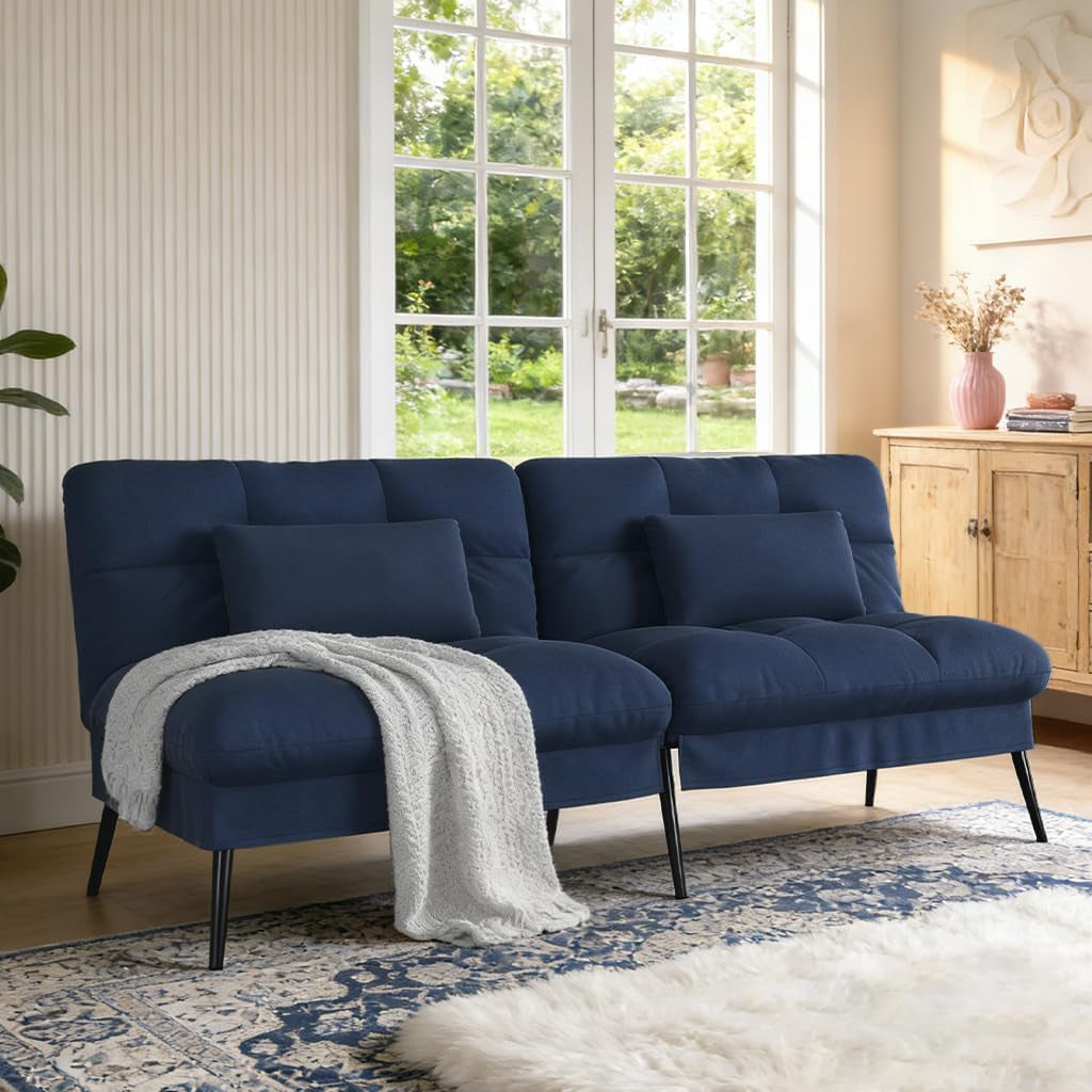 Navy blue fabric futon sofa with two lumbar pillows and a draped knit throw in a sunny living room.