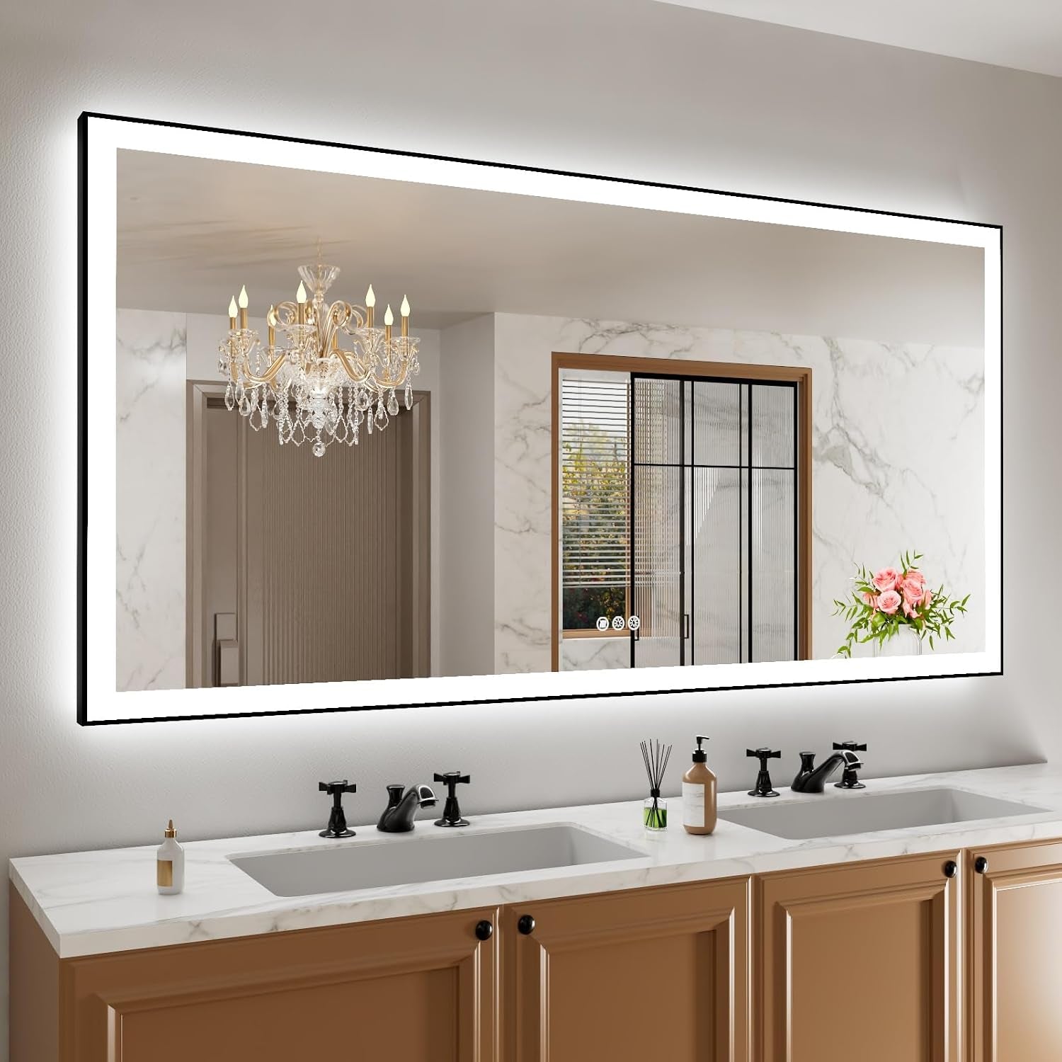Wide horizontal backlit mirror above a double-sink vanity reflecting a chandelier and window.